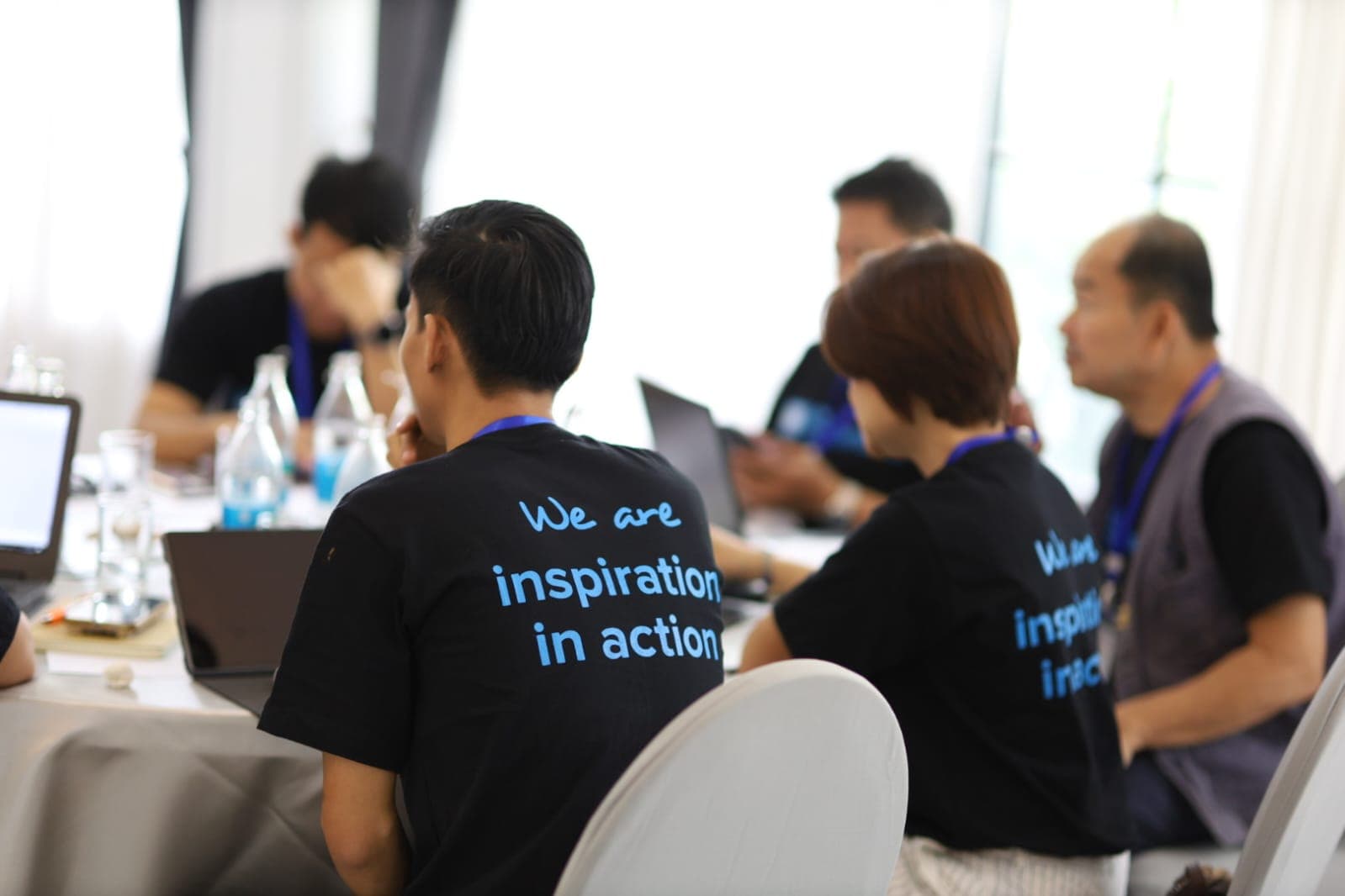 People in black shirts with 'We are inspiration in action' text sit at a table.